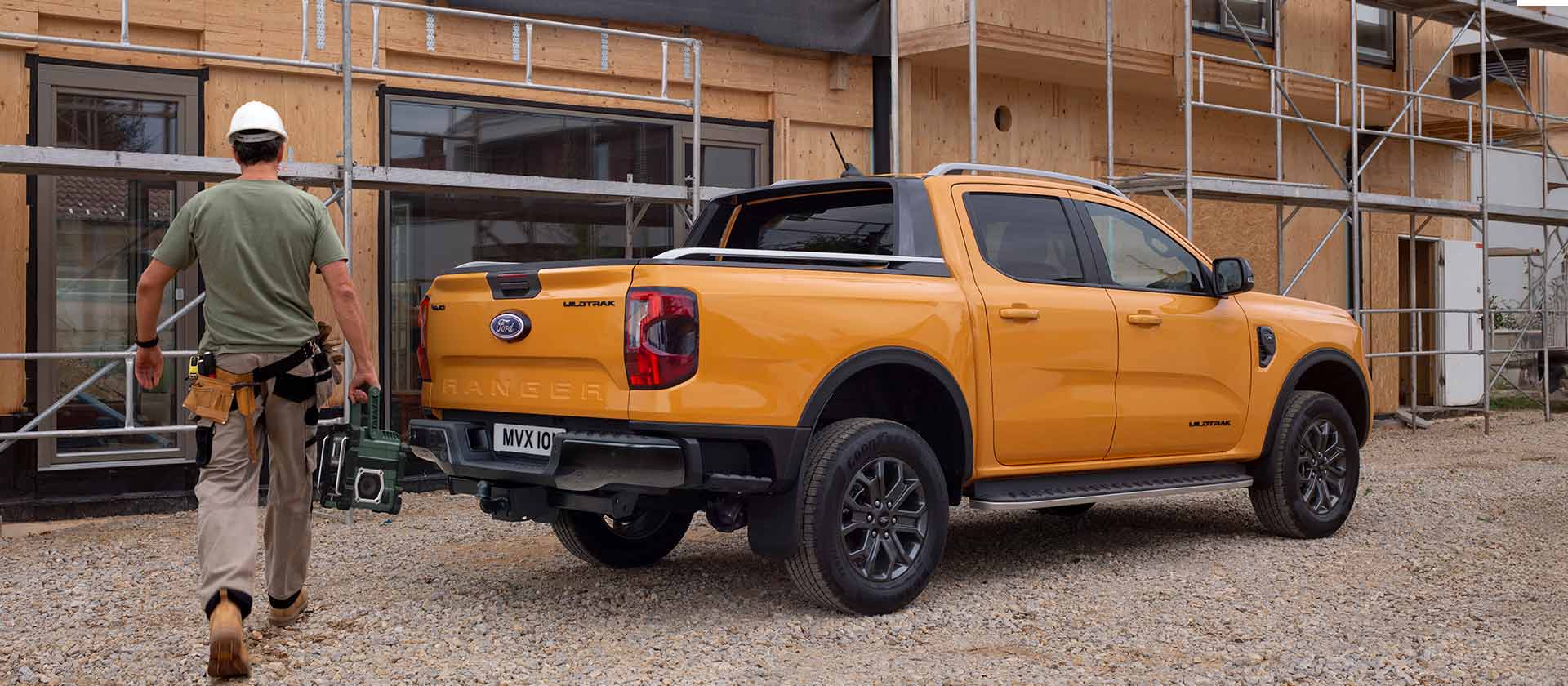 Suojakypärää käyttävä työntekijä kävelemässä kohti keltaista Ford Ranger -avolava-autoa rakennustyömaalla.