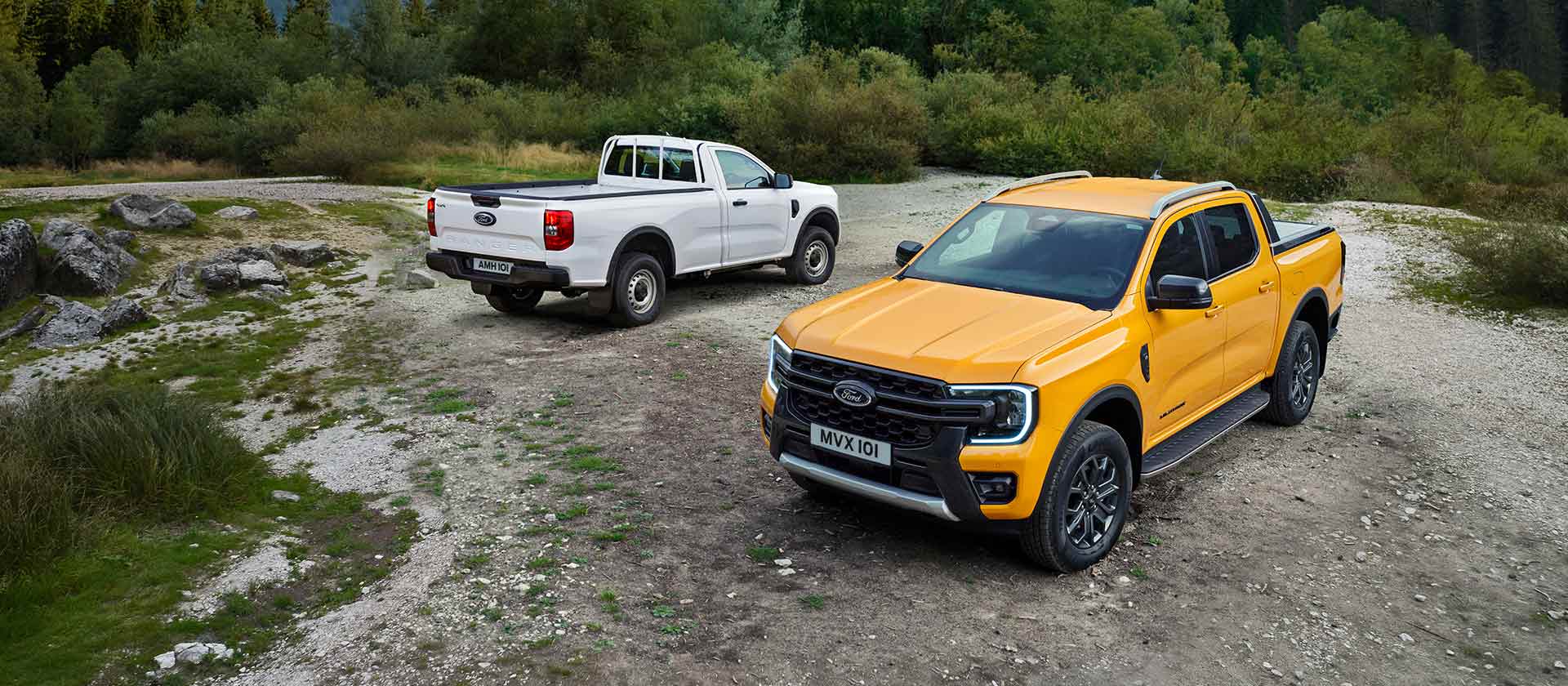 Valkoinen Ford Ranger ja keltainen Ford Ranger pysäköityinä kivisessä maastossa tien sivussa. 