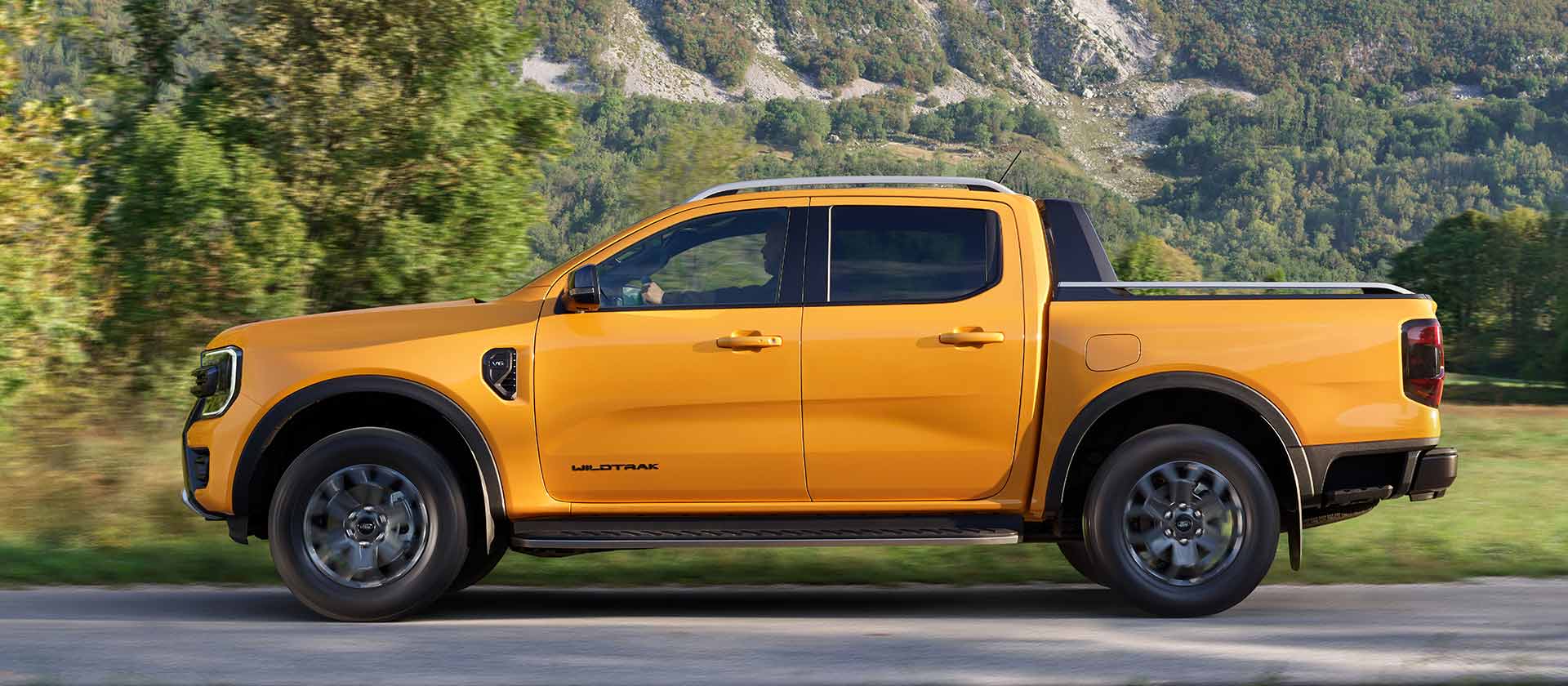 Sivuprofiilikuva keltaisesta Ford Ranger Wildtrak Double Cabista pysäköitynä tien sivuun vuoristomaisemassa.