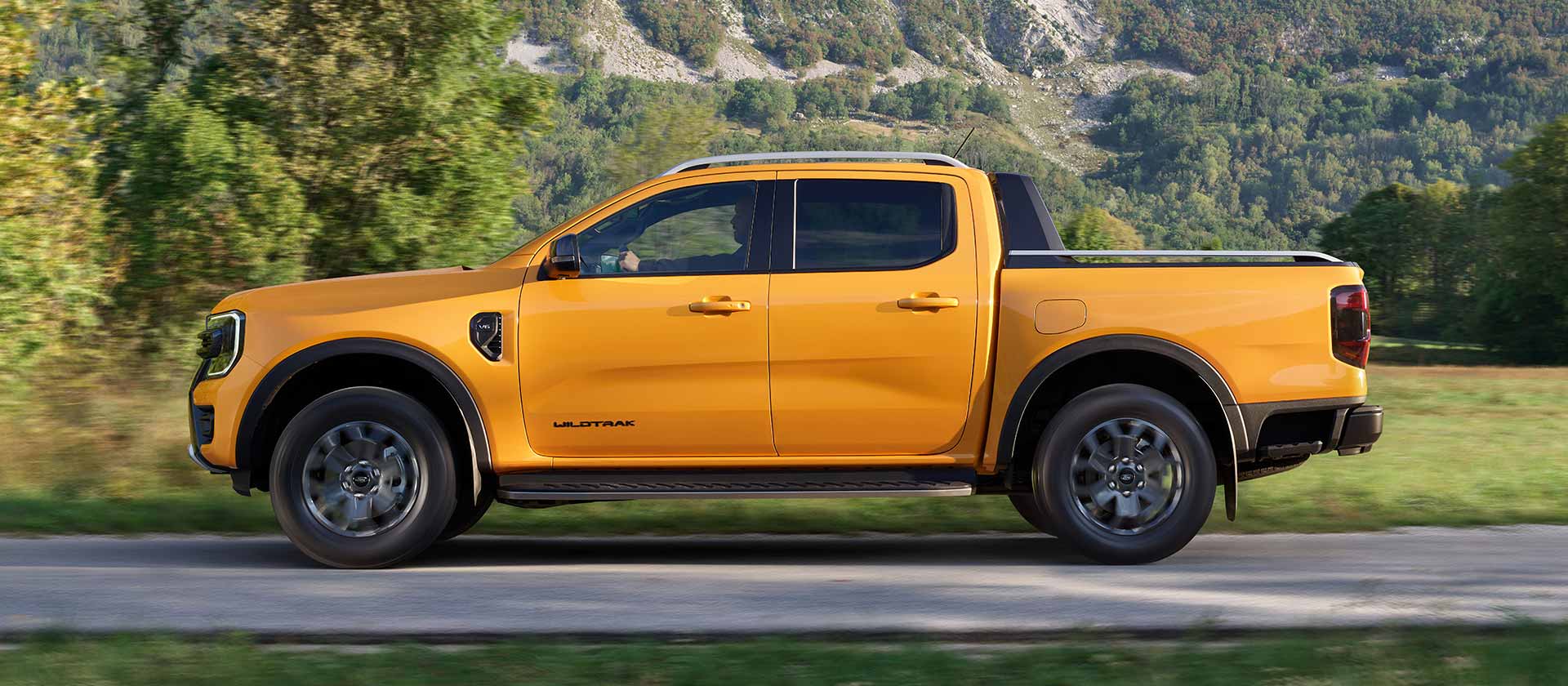 Sivunäkymä päällystettyä tietä pitkin ajavasta keltaisesta Ford Ranger Wildtrakista.