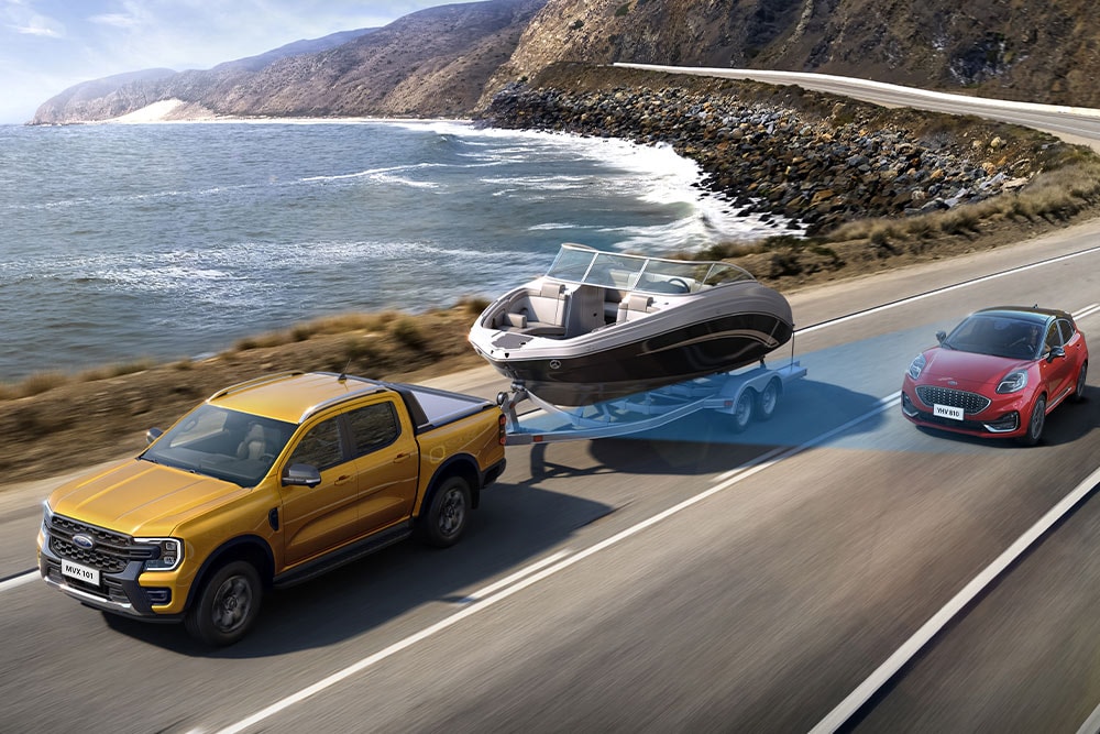 Keltainen Ford Ranger vetää peräkärryssä venettä ajettaessa rannikkotietä osoituksena Rangerin vetokyvystä.