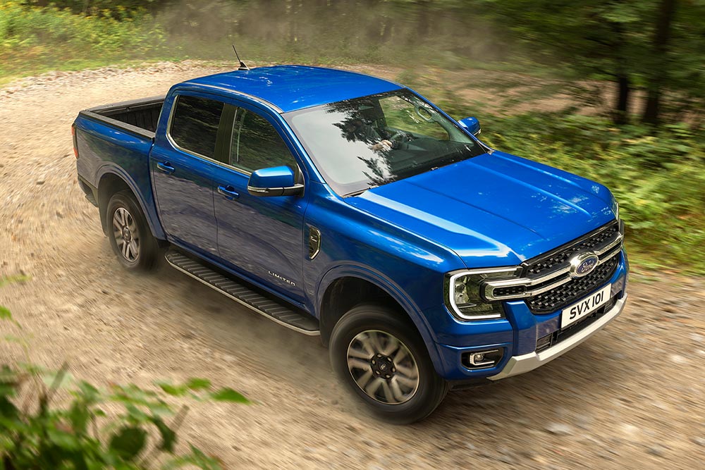 Sininen Ford Ranger -avolava-auto ajamassa metsäisellä hiekkatiellä pölyä nostattaen.