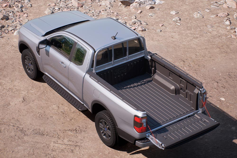 Ylhäältä kuvattu hopeanharmaa Ford Ranger XLT Super Cab pysäköitynä hiekkamaastoon takalaita alaslaskettuna.