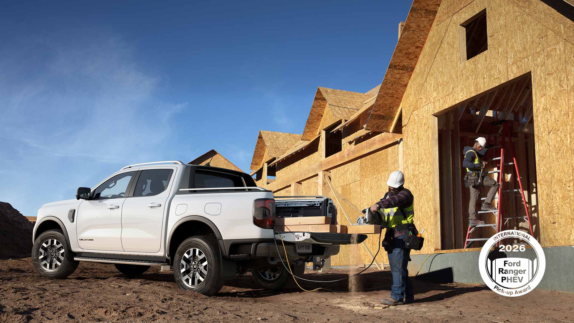 Valkoinen Ford Ranger pick-up on pysäköitynä rakennustyömaalle, ja se toimii virranlähteenä sahalle, jolla rakennustyöntekijä katkaisee puulankkua.