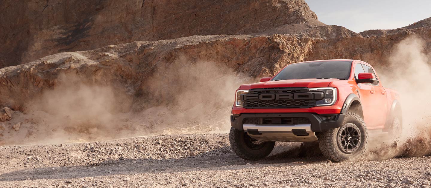 Punainen Ford Ranger Raptor lennättää pölyä ajaessaan aavikkomaisemassa.