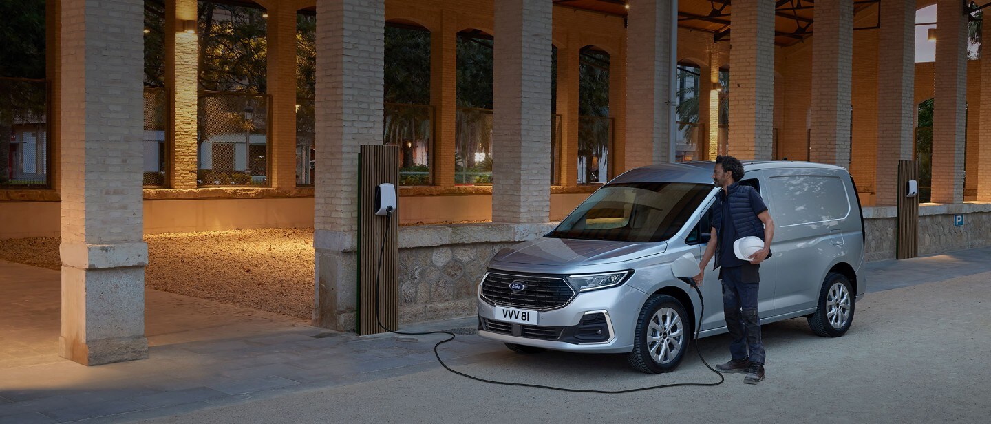 Mies, jolla on suojakypärä, kytkee latauslaitteen kaapelin täysin uuteen Stardust Silver -väriseen Ford Transit Connectiin.
