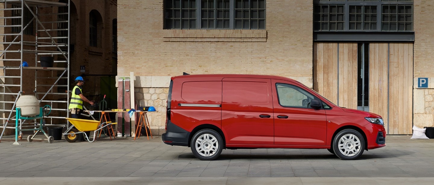 Täysin uusi Maple Red -värinen Ford Transit Connect, jossa näkyy sivuliukuovi, pysäköitynä rakennustyömaalle.