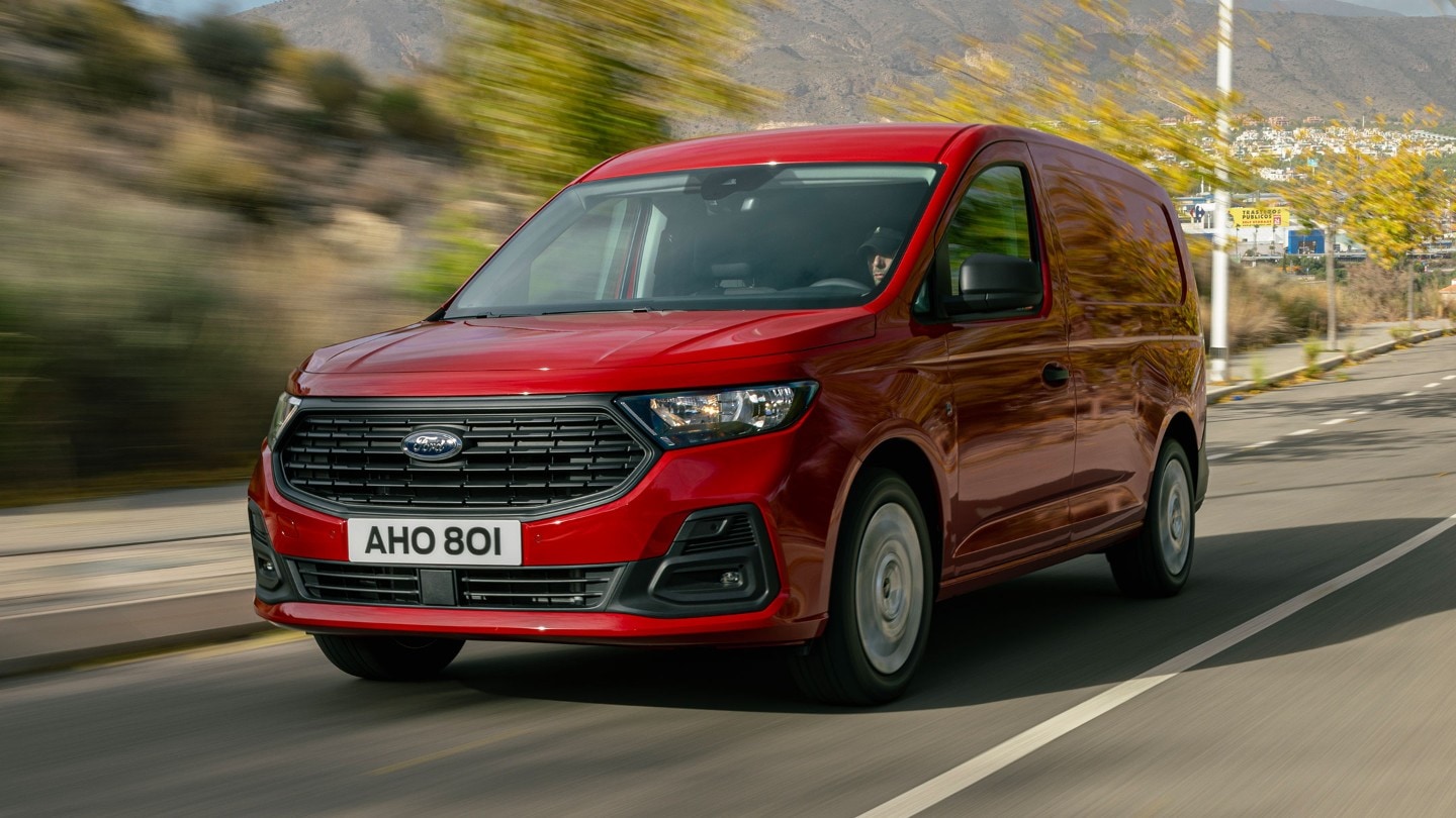 Täysin uusi Maple Red -värinen Ford Transit Connect ajaa tietä pitkin esitellen etusäleikköä ja ajovaloja. 