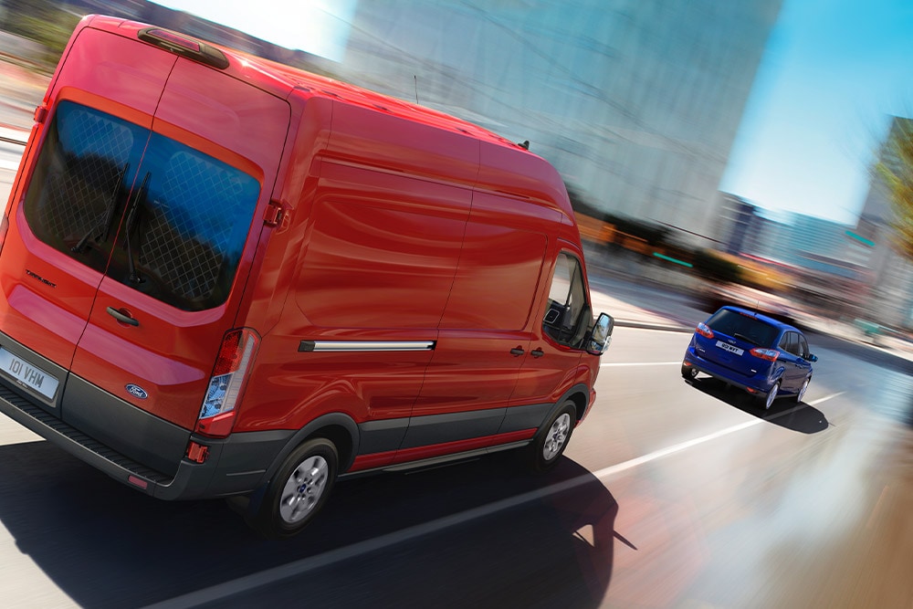 Punainen Ford Transit -pakettiauto ajamassa tiellä.