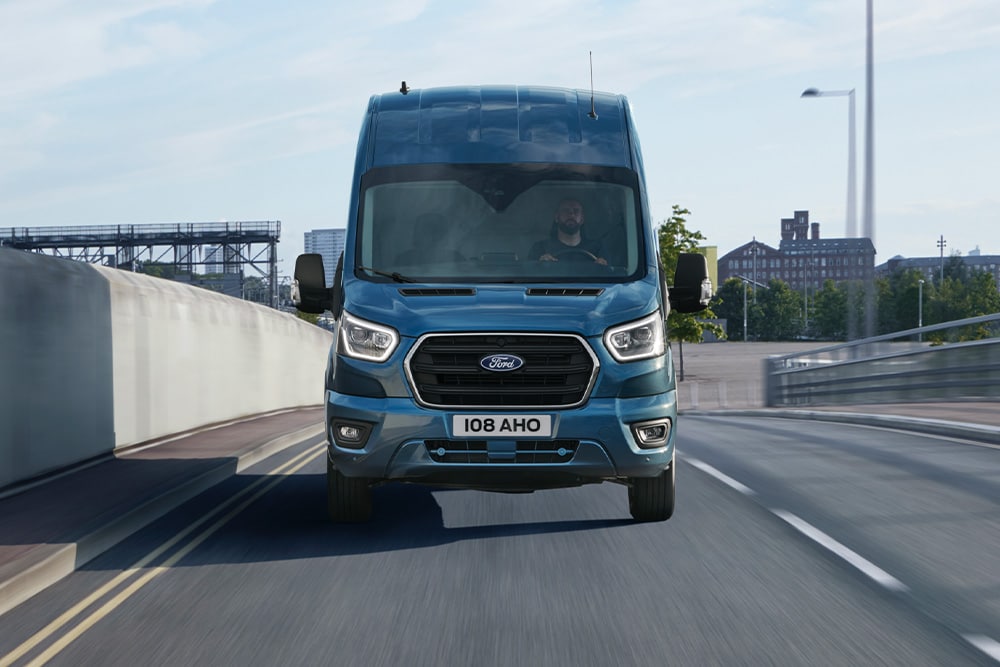 Sininen Ford Transit Van edestä kuvattuna ajamassa tiellä. 