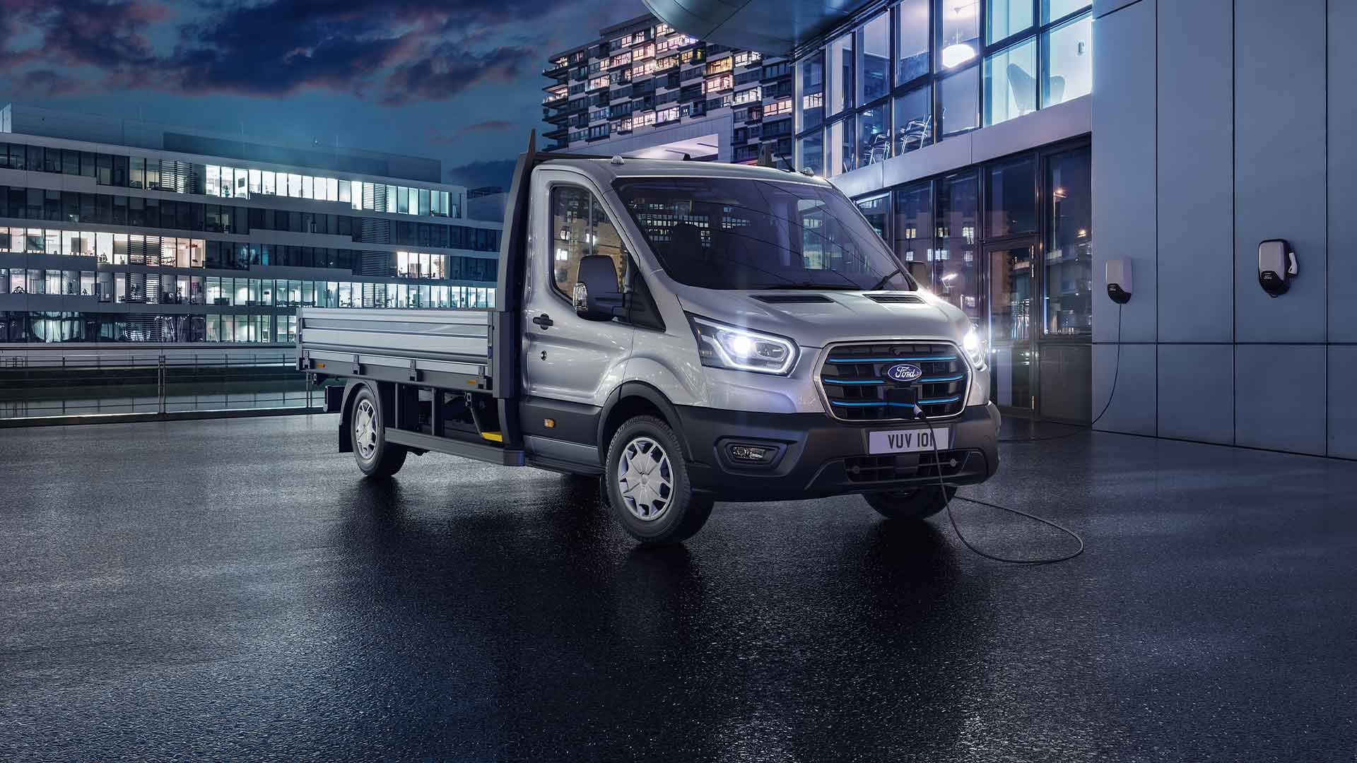 Hopeanvärinen Ford Transit Chassis Cab pysäköitynä modernin rakennuksen eteen iltamyöhään.