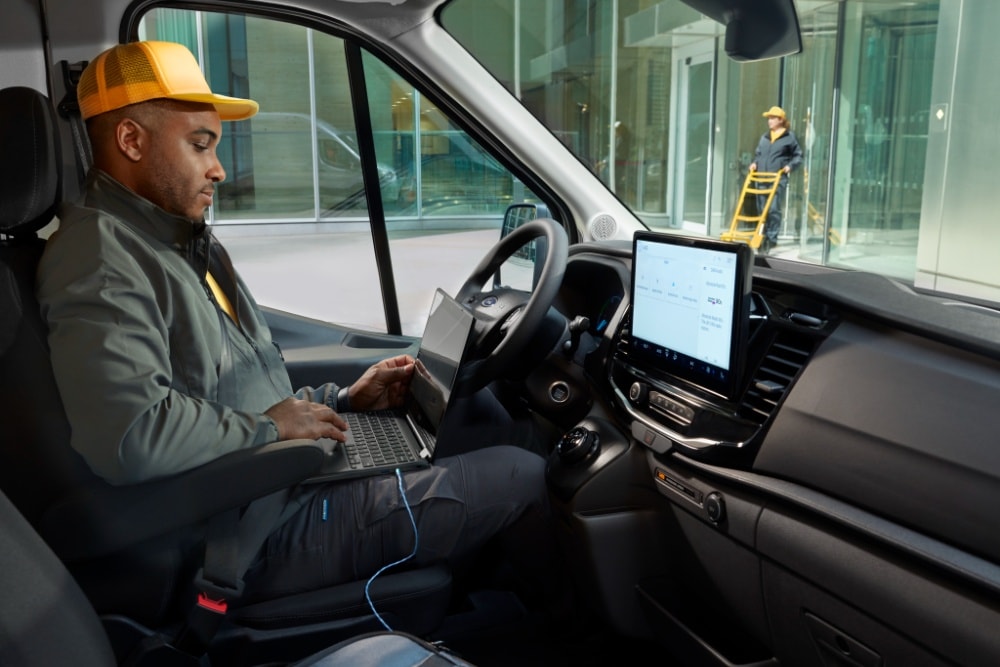 Kannettavaa tietokonetta käyttävä mies Ford Transit -pakettiauton kuljettajan paikalla.