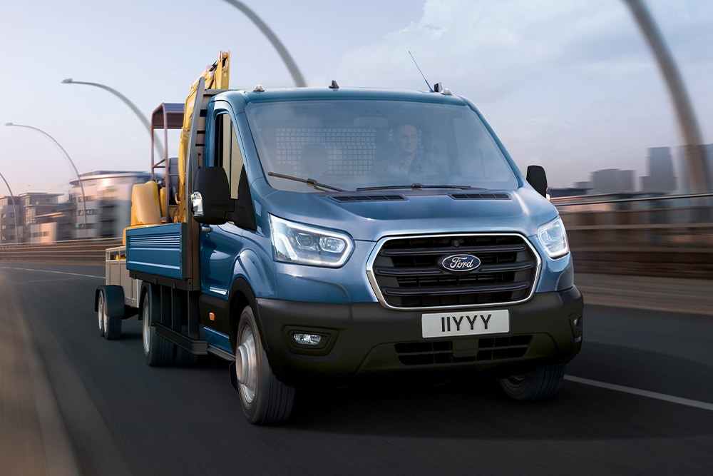 Kuva kaupungissa ajavan Ford Transit Chassis Cabin etusäleiköstä; kuormana kaivuri. 