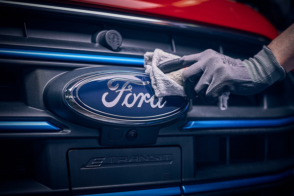  Käsineessä oleva käsi koskettaa Ford-merkkiä ajoneuvon etusäleikössä.
