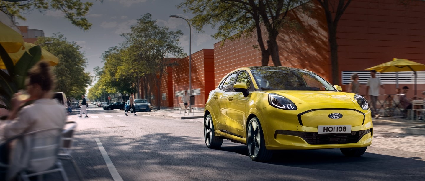 Keltainen sähköinen Ford Puma Gen-E® edestä kuvattuna ajamassa kaupungin kadulla.