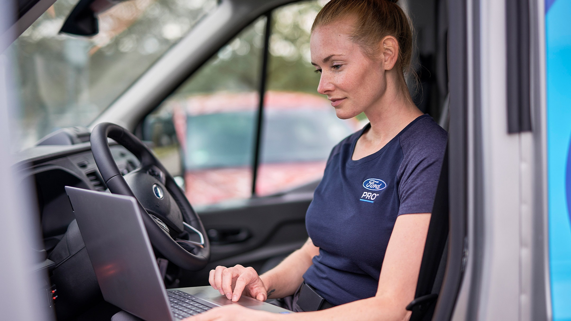 Ford Pro -asiantuntija istui autossa tarkistamassa kannettavaa tietokonetta Ford-ajoneuvohuollon aikana. 