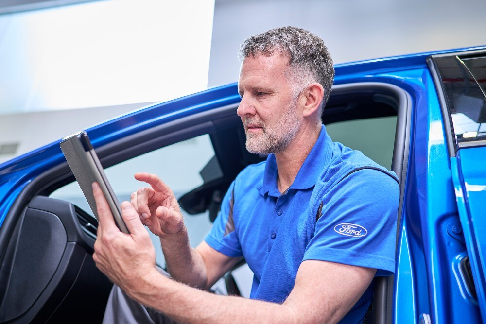 Ford-teknikko istuu sinisessä Ford-ajoneuvossa ja käyttää tablettia ajoneuvojärjestelmien tarkistamiseen.