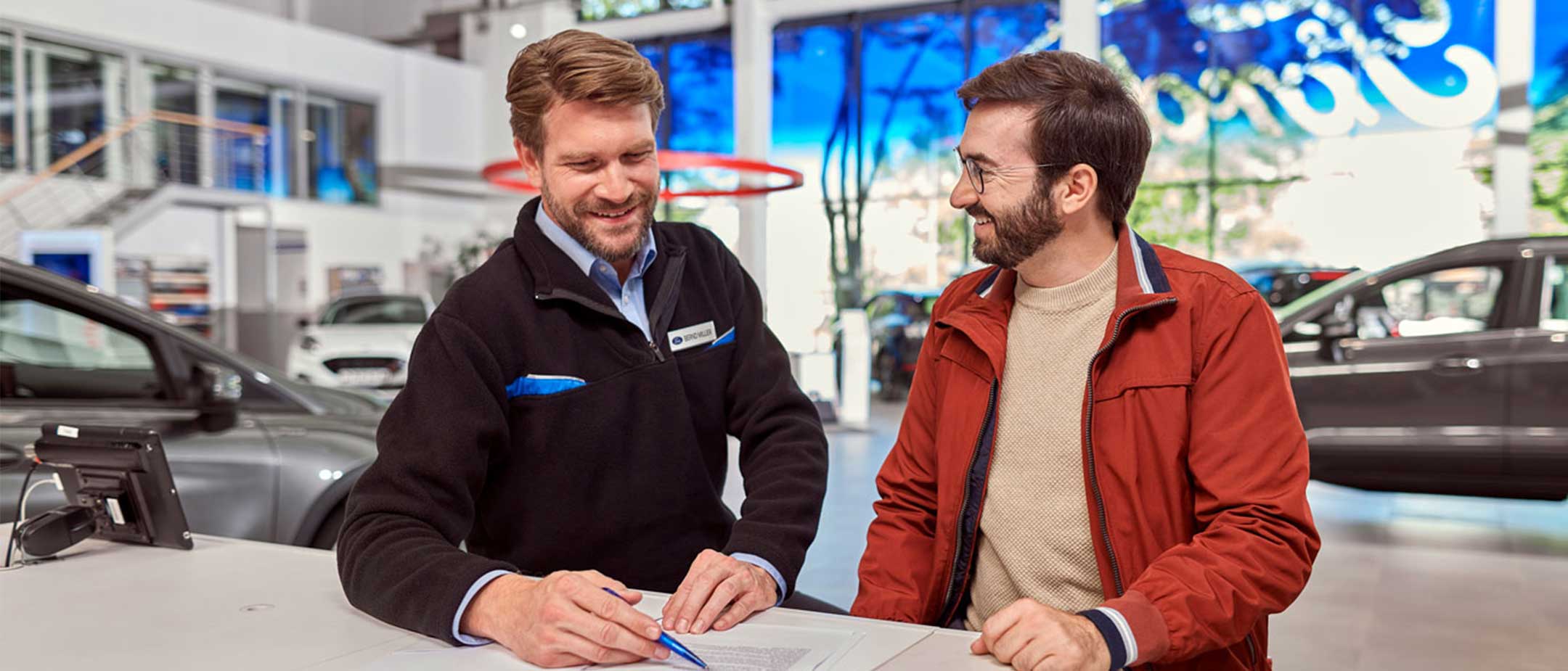 Ford-myyjä ja asiakas katsovat papereita iloisesti