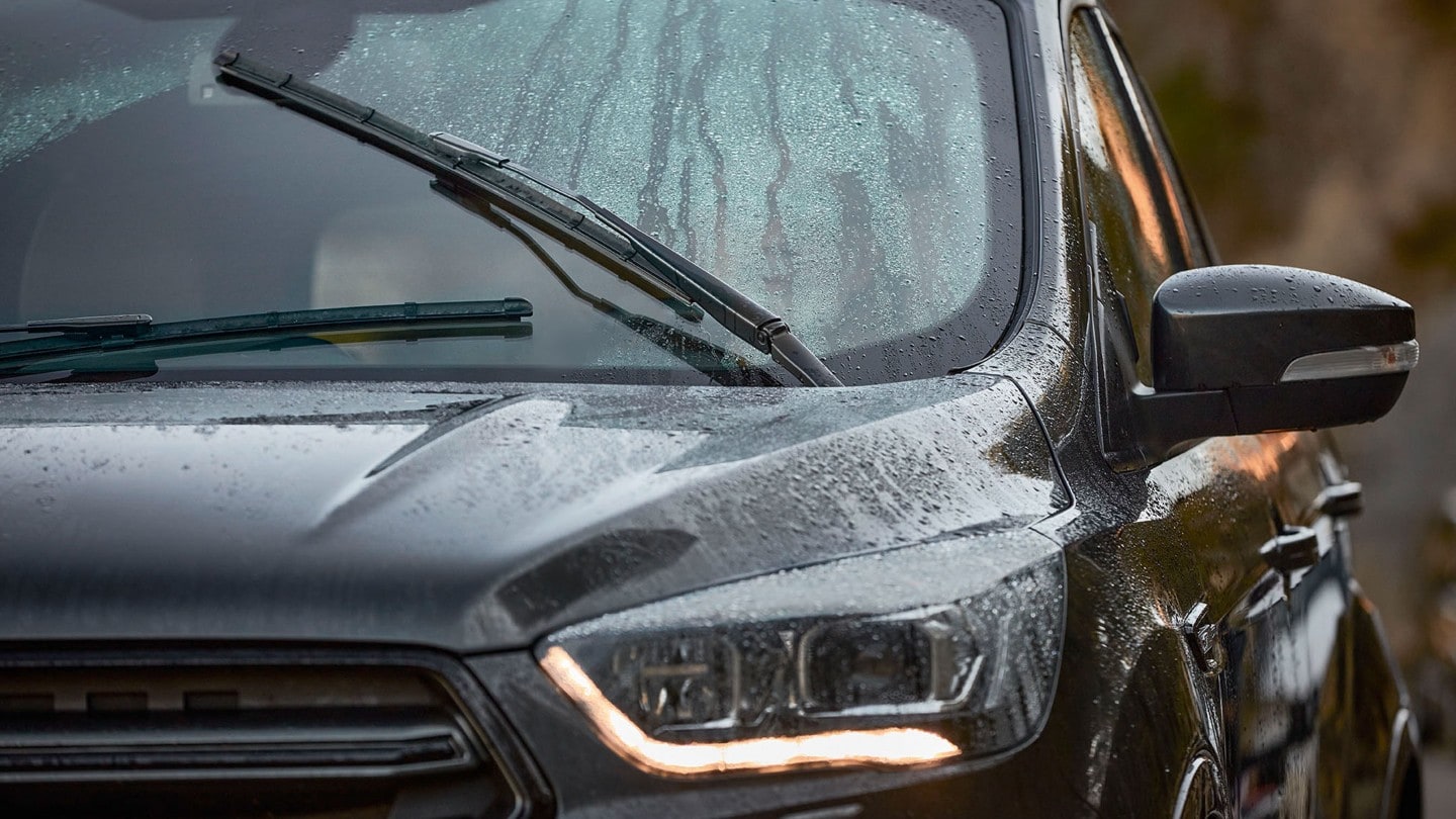 Lähikuva tumman Ford-ajoneuvon etuosasta, tuulilasissa näkyy sadepisaroita ja pyyhkijä. Lähikuva tumman Ford-ajoneuvon etuosasta, tuulilasissa näkyy sadepisaroita ja pyyhkijä.
